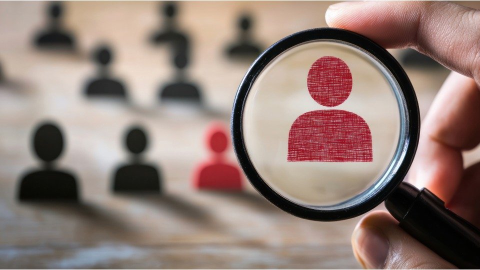 Loupe mettant en évidence une silhouette rouge parmi des silhouettes noires, symbolisant la prise en compte des besoins spécifiques des clients par une agence web