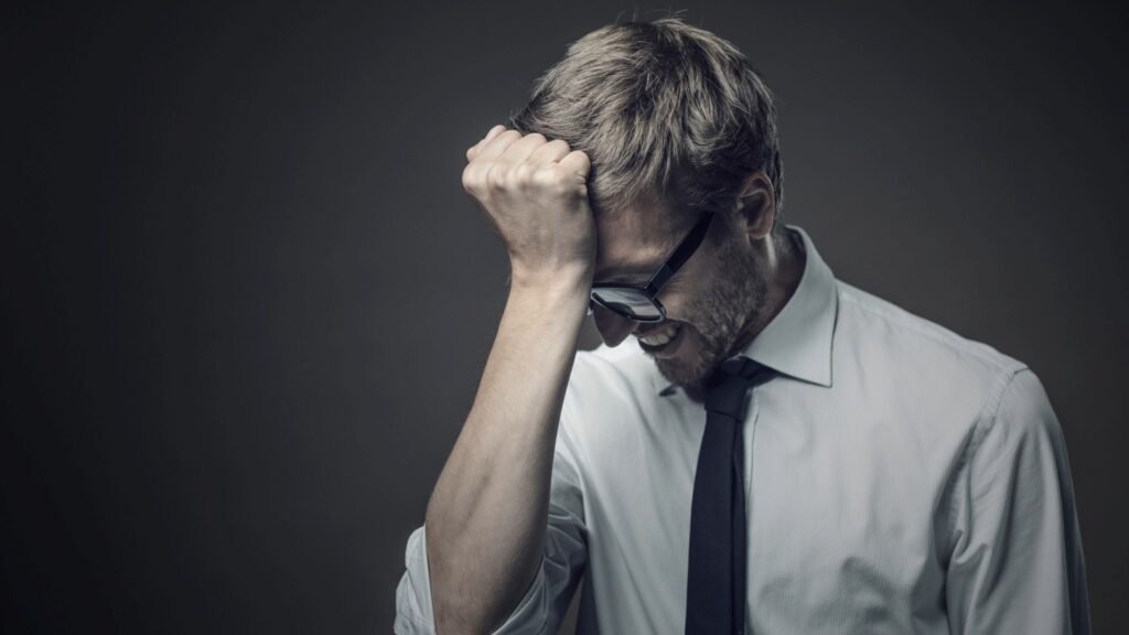 Homme en chemise blanche et cravate noire, poing fermé contre son front, symbolisant les erreurs à éviter lors de la création d’un site internet pour PME et TPE.