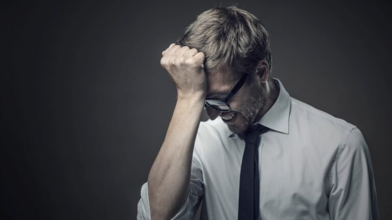 Homme en chemise blanche et cravate noire, poing fermé contre son front, symbolisant les erreurs à éviter lors de la création d’un site internet pour PME et TPE.
